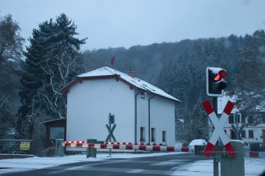 Rhineland Palatinate, Germany - February 8, 2021: Red light at railroad crossing with bars down in a small German village on a cold, snowy grey winter day.