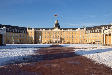 Karlsruhe, Almanya - 12 Şubat 2021: Almanya 'da güneşli bir kış öğleden sonrasında Karlsruhe Sarayı' nın ön tarafına uzanan karla çevrili yürüyüş yolu.