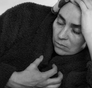 Kafasında ıslak bir bezle, bornoz giyen orta yaşlı hasta bir kadın..