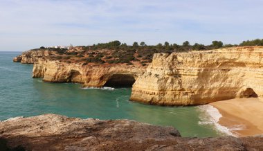 Portekiz 'in Algarve kentindeki Seven Hanging Vadisi boyunca güneşli bir kış gününde, Atlantik Okyanusu ve kireçtaşı kayalıklarıyla çevrili küçük kumlu sahil..
