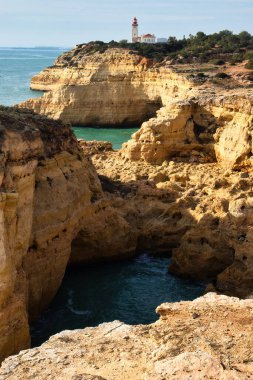 Carvoeiro, Portekiz - 25 Aralık 2019: Güney Portekiz 'de güneşli bir kış gününde Farol De Alfanzina Deniz Feneri ile Atlantik Okyanusu' ndaki kireçtaşı kayalıkları.