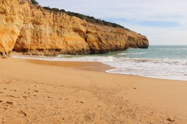 Atlantik Okyanusu 'nun yanındaki kumsalda güneşli bir kış gününde Portekiz' in güneyindeki Seven Hanging Vadisi 'nde kireçtaşı uçurumu var..