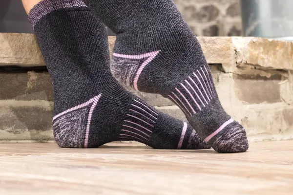 Pointed toe on feet with warm grey and pink socks in front of a stone wall.