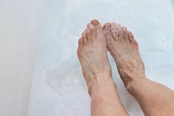Water spraying on top of feet in a white bath with bubbles.