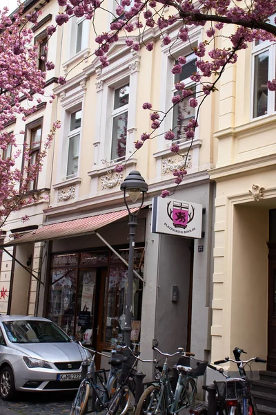 stock image Bonn, Germany - April 16, 2021: Bicycles and car parked outside a shop in a yellow building under pink cherry blossoms on a spring day in Bonn, Germany.