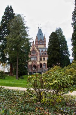 Konigswinter, Almanya - 16 Nisan 2021: Almanya 'nın Konigswinter şehrinde bir bahar günü Drachenburg kalesi etrafındaki yeşil çimenler ve ağaçlar.