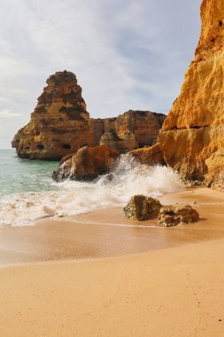 Sıcak bir kış gününde Portekiz 'in güneyindeki kumlu bir sahilde kayaların üzerinden su sıçrıyor..