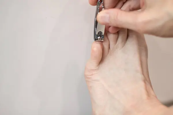 Clipping pinkie toenail with silver nail clippers against a white background.