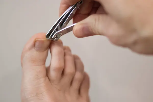 Clipping toenail on a big toe on a right foot against a white background.