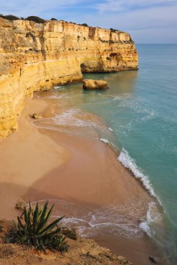Güney Portekiz 'de güneşli bir kış gününde etrafı su ve uçurumla çevrili kumlu bir sahil manzarası..