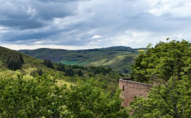 Güneş, bulutlu bir bahar gününde Almanya 'nın Bad Munster kentindeki bir tepenin yakınındaki bir kalenin yanındaki ağaçların üzerinde parlıyor..