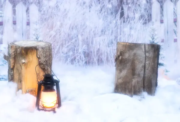 Lantern sitting in fake snow in front of a log with a winter background.