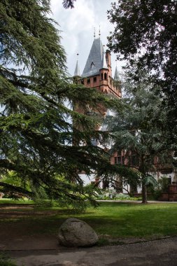 Weinheim, Almanya - 19 Mayıs 2021: Weinheim, Almanya 'da bir bahar gününde arka planda kahverengi kule bulunan parktaki ağaçlar.