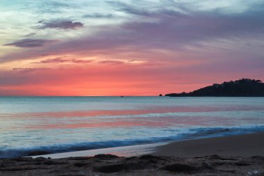 Kum plajı ve okyanus. Güney Portekiz 'de bir kış akşamı günbatımında arka planda binaları olan bir tepe..
