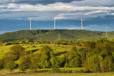 Winnweiler, Almanya 'da bir bahar akşamında üç rüzgar türbini olan bir tepede parlayan güneş..