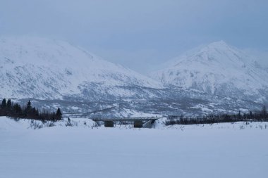 Alaska 'daki Castner Mağarası' nın yakınlarında soğuk bir kış günü, arka planda dağlarla Richardson Otoyolu 'ndaki köprü..