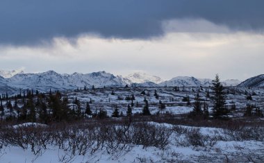 Alaska 'da bir kış günü, dağlardaki kara bulutların arasından parlayan güneş..
