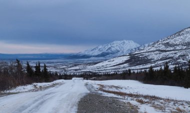 Alaska 'da bir kış öğleden sonra ağaçların ve dağların arasından geçen buzlu yol..