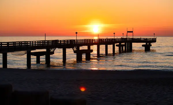 stock image Sun setting behind a pier at the Baltic Sea on a spring night in northern Germany.