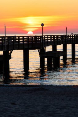 Kuzey Almanya 'da bir bahar gecesi Baltık Denizi' nde bir rıhtımın arkasında güneşli bir gökyüzünde batıyor..