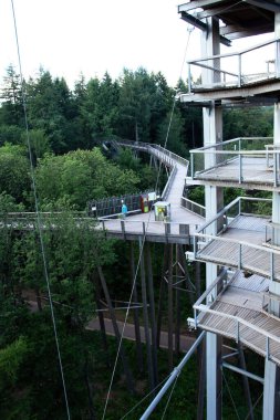 Mettlach, Almanya - 27 Haziran 2021: Almanya 'da güneşli bir ilkbahar öğleden sonrasında Saarschleife' de ağaçların tepesinde yürüyüş yapan kulenin yanı ve ahşap yürüyüş yolu.