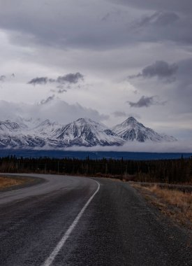 Mountains behind Alaska Highway and trees on a dark autumn day in Canada.  clipart