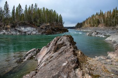 Kanada 'da bulutlu bir sonbahar gününde Alaska Kanada Otobanı' nda renkli nehrin yanında kayalar. 