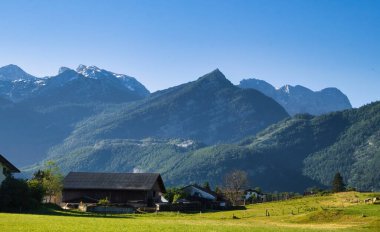 Sun shining on mountains behind houses in Golling an der Salzach, Austria on a spring morning. clipart