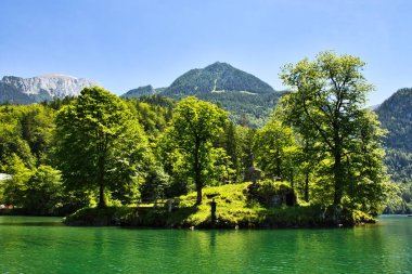 Schonau am Konigssee, Almanya - 15 Haziran 2021: Almanya 'da güneşli bir bahar gününde Konigssee' de yeşil ağaçlarla çevrili heykel.