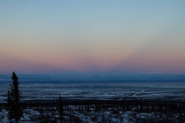 Delta Junction, Alaska yakınlarında bir kış günü, Coloful güneşi bulutların içinden ışıldar.. 