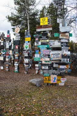 Watson Lake, Kanada - 9 Ekim 2024: Bir bahar günü Kanada 'da Alaska Otoyolu' ndaki TabelaPost Ormanı 'nda ahşap levhalar üzerinde renkli tabelalar ve plakalar. Gönderilerdeki renkli işaretler 
