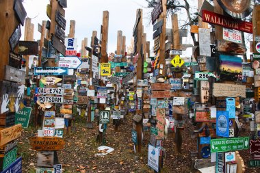 Watson Lake, Canada - October 9, 2024: Signs on wood posts at Sign Post Forest on the Alaska Highway in Canada on a spring day.  clipart