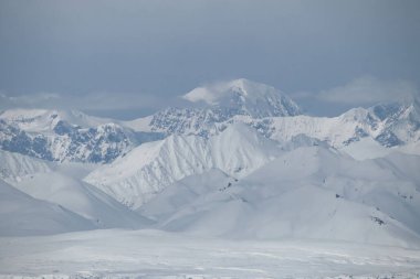 Alaska 'nın iç kesimlerindeki Denali Otobanı' nda beyaz bir bahar gününde bulutlarla kaplı dağların tepelerinde parlayan güneş.. 