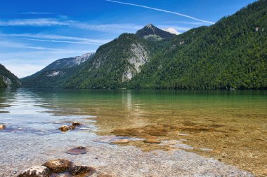 Almanya 'nın Bavyera kentindeki güneşli bir bahar gününde Konigssee' de kayalar ve arka planda dağlar..