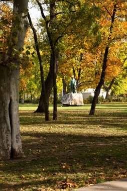 Budapeşte, Macaristan - 26 Ekim 2021: Macaristan 'ın Budapeşte kentinde bir sonbahar günü, bir parktaki renkli ağaçlarla çevrili bir heykel üzerinde güneş parlıyor.