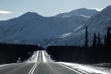 Alaska 'nın iç kesimlerinde güneşli bir kış gününde Richardson otoyolunun arkasındaki dağların tepesinde kar esiyor.. 