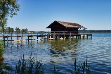 Bavyera, Almanya - 17 Haziran 2021: Güney Almanya 'da güneşli bir bahar gününde Chiemsee' de köpek dostu bir plajda liman ve ahşap bina.