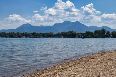 Bavyera, Almanya - 17 Haziran 2021: Güney Almanya 'da güneşli bir bahar gününde, arkasında dağlar olan Chiemsee' deki Rocky plajı.