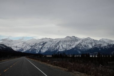 Alaska otobanındaki gölün arkasındaki güzel karlı dağlar Kanada 'da bulutlu bir sonbahar günü. 