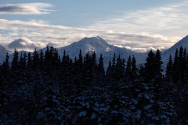 Delta Junction, Alaska yakınlarında bir kış öğleden sonra dağların arkasında mavi gökyüzünde beyaz bulutlar.