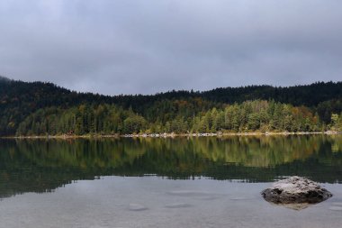 Almanya 'nın Bavyera şehrinde bulutlu bir sonbahar gününde ağaçlar ve onların Eibsee' deki sudaki yansımaları. 
