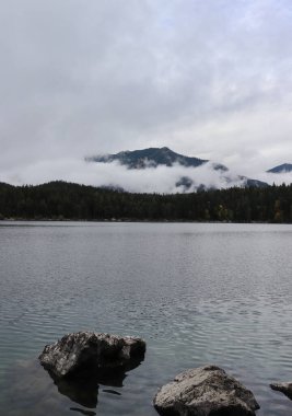 Almanya 'nın Bavyera kentindeki Eibsee' de bulutlu bir sonbahar gününde bir dağın önünde sis var.. 