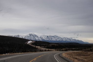 Kanada 'da bulutlu bir sonbahar gününde arka planda dağlar olan Hilly Alaska Otoyolu.