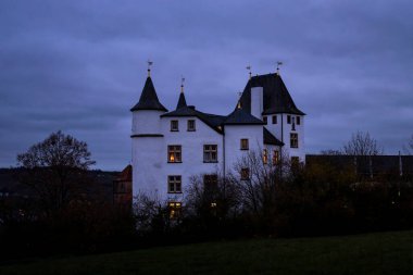 Nennig, Almanya - 19 Kasım 2021: Almanya 'da bulutlu bir sonbahar akşamında Victor' s Residenz Hotel Schloss Berg 'in camlarında ışıklar.