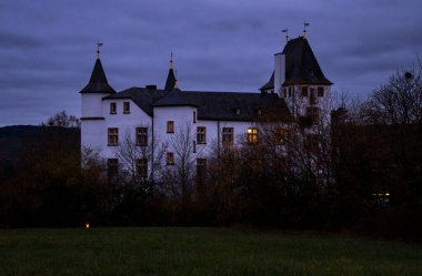 Nennig, Almanya - 19 Kasım 2021: Victor 's Residenz Hotel Schloss Berg Almanya' da bulutlu bir sonbahar gecesinde ağaçların arkasında.