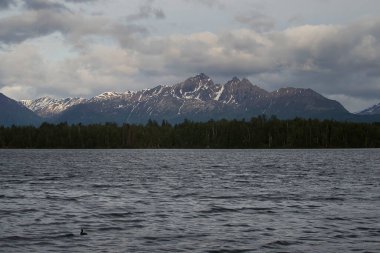 Wasilla, Alaska 'da bulutlu bir bahar gününde Lucille Gölü' nün arkasındaki dağlarda parlayan güneş..