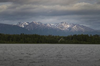 Wasilla, Alaska 'da bulutlu bir bahar gününde Lucille Gölü' nün arkasındaki dağın tepesinde güneş parlıyor..
