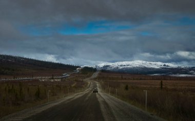Alaska 'da bulutlu bir bahar gününde Dalton Karayolu' nun yanındaki boru hattı ve binalar. 