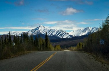 Alaska 'da güneşli bir bahar gününde Dalton otoyolunun asfaltlı kısmının arkasındaki dağlar. 