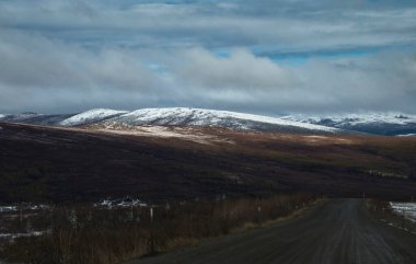 Alaska 'da bulutlu bir bahar gününde Dalton Otoyolu' nun yanındaki tepelerde parlayan güneş.. 
